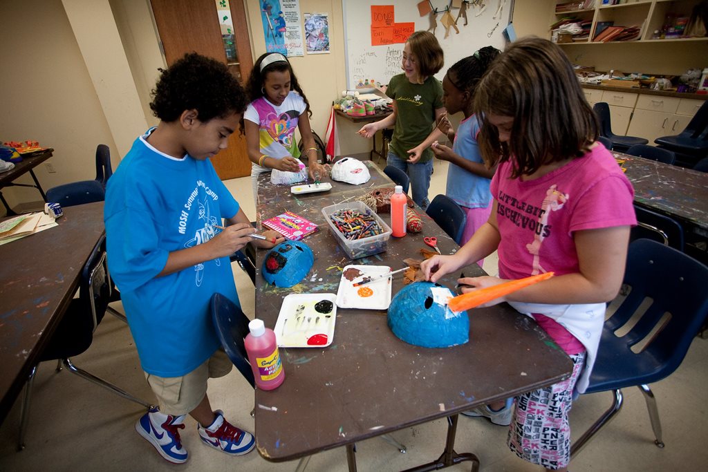 middle school children gathered around a tale engaged in an arts and crafts painting activity