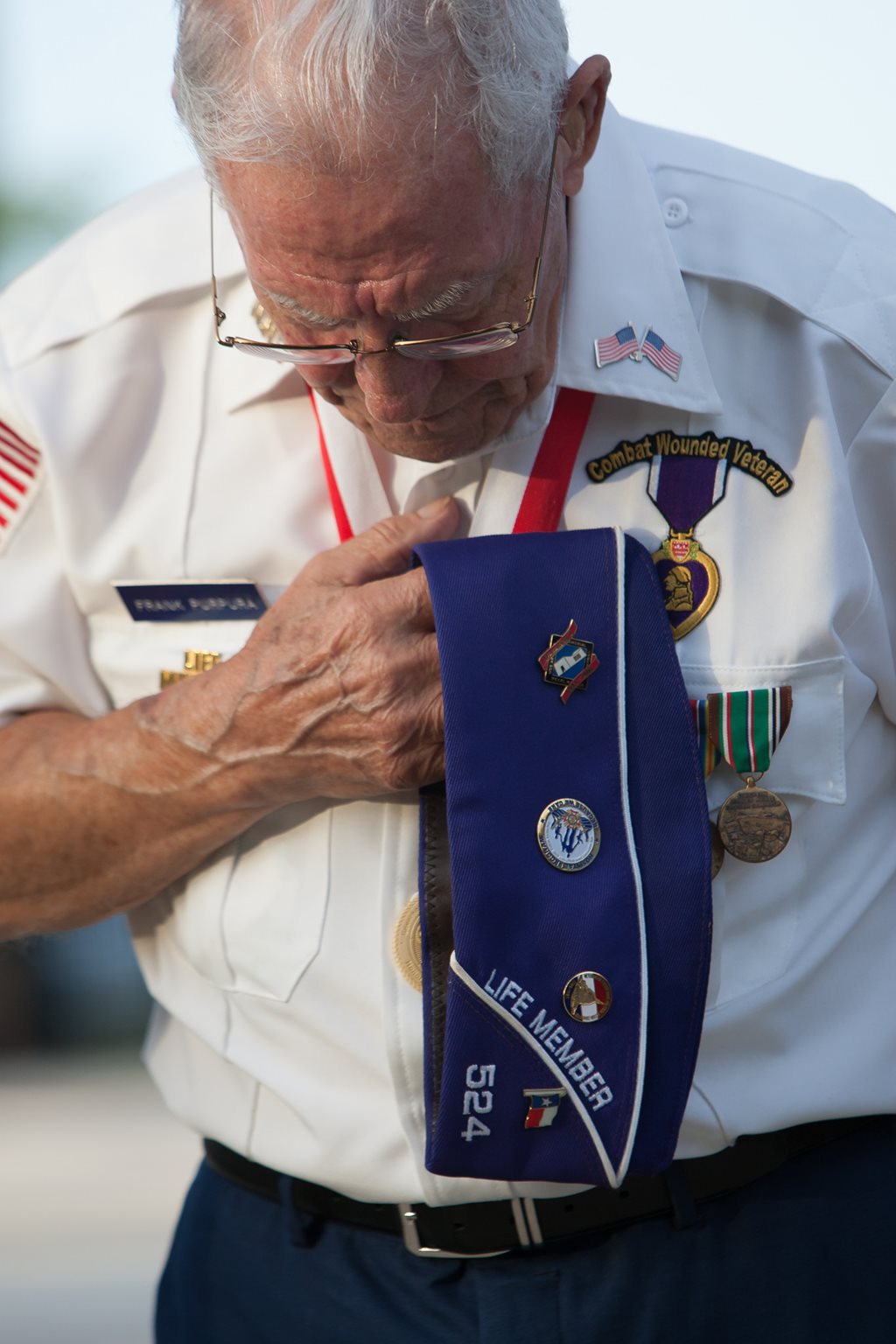 An elderly member of the Military Order fo the Purple Heart bows his head and places his hand over his heart.
