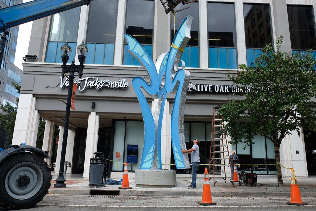 construction crew installing large blue abstract flower sculpture on sidewalk