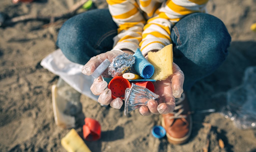 child's hands picking up plastic garbage on the beach