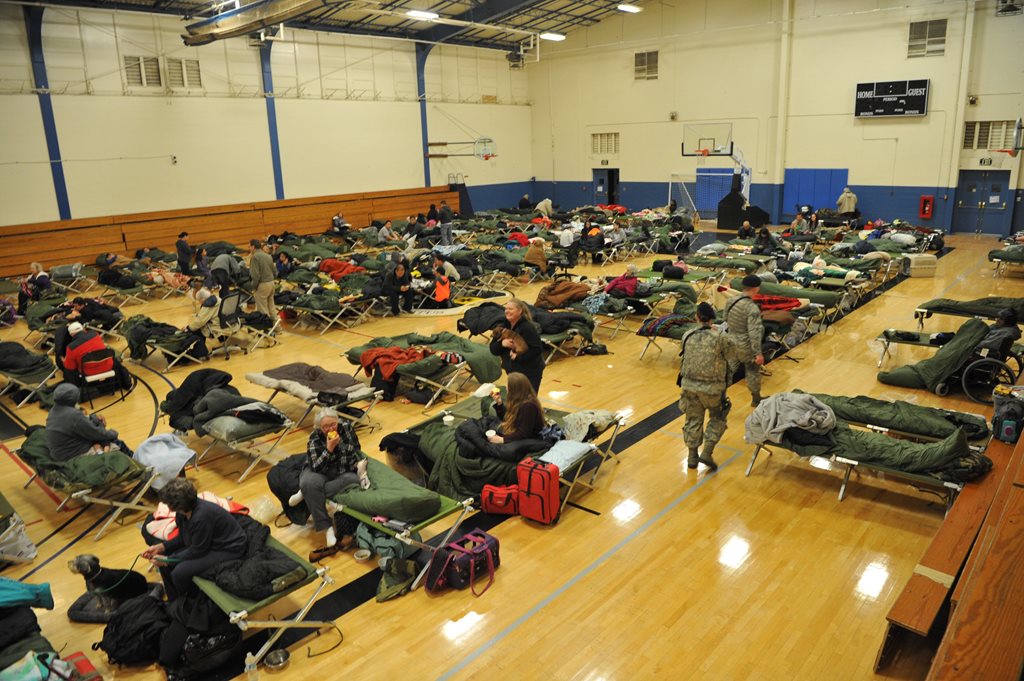people sleeping on cots in an evacuation shelter