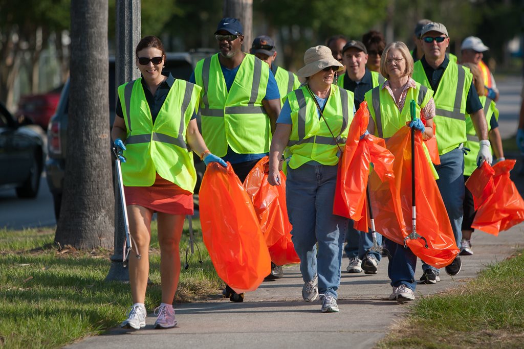 Cleanup participants dressed in reflective vests collect trash in bright orange garbage bags