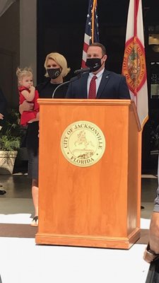 Photo of Council Member Carrico speaking at the podium in front of city hall accompanied by his wife Shawnelle and daughter Monroe.