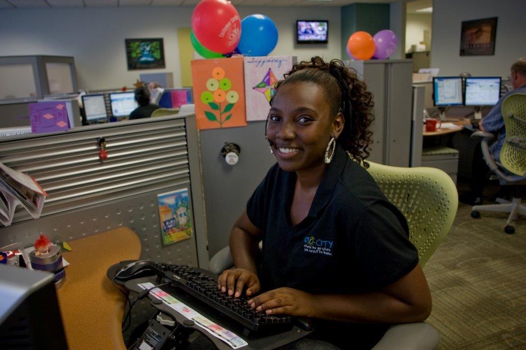 630-CITY Call Center Employee at a Computer Smiling Into Camera