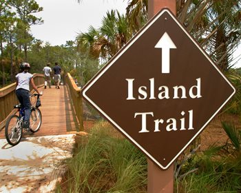 Island trail opening with sign and people on bikes and walking at start of trail
