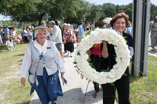 Photo of Lyn Corley carrying a white wreath to be placed to honor the French Huguenot colonist of La Caroline.